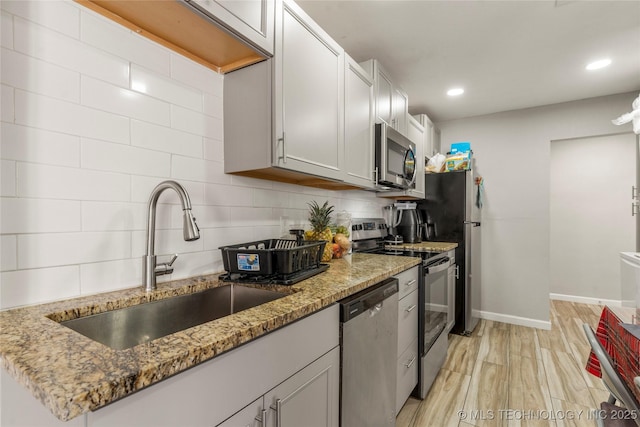 kitchen featuring baseboards, light wood-type flooring, decorative backsplash, appliances with stainless steel finishes, and a sink