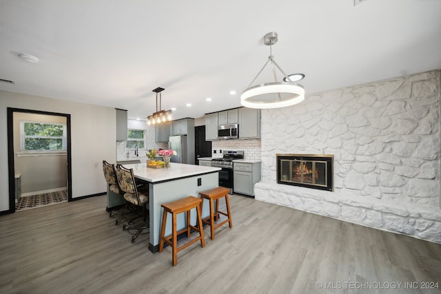 kitchen with a breakfast bar area, gray cabinets, pendant lighting, stainless steel appliances, and backsplash