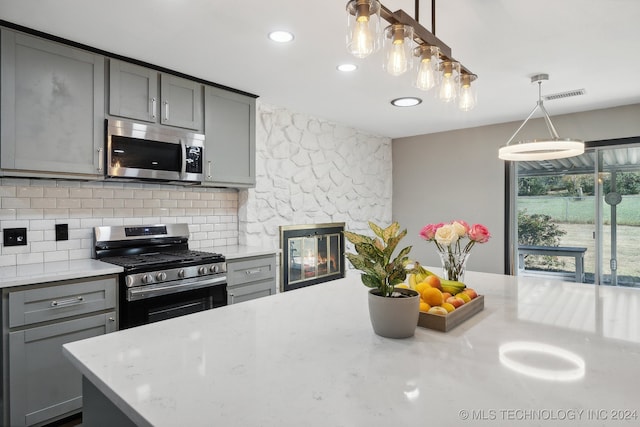 kitchen with gray cabinetry, hanging light fixtures, stainless steel appliances, a fireplace, and decorative backsplash