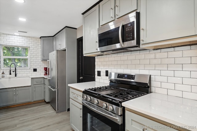 kitchen featuring stainless steel appliances, gray cabinets, sink, and decorative backsplash