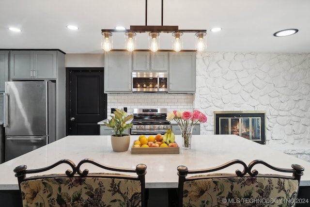 kitchen featuring backsplash, decorative light fixtures, gray cabinets, and stainless steel appliances