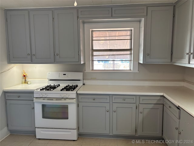 kitchen featuring white range with gas stovetop, light tile patterned flooring, and gray cabinetry