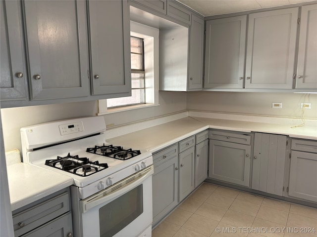 kitchen with light tile patterned floors, white gas range, and gray cabinetry