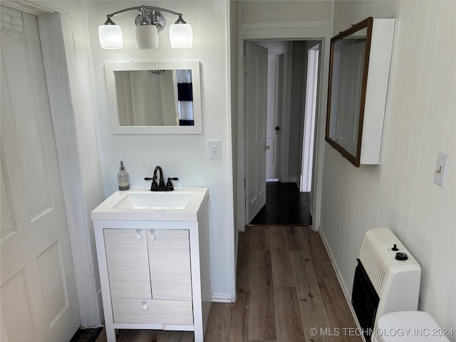 bathroom featuring toilet, heating unit, wooden walls, hardwood / wood-style flooring, and vanity