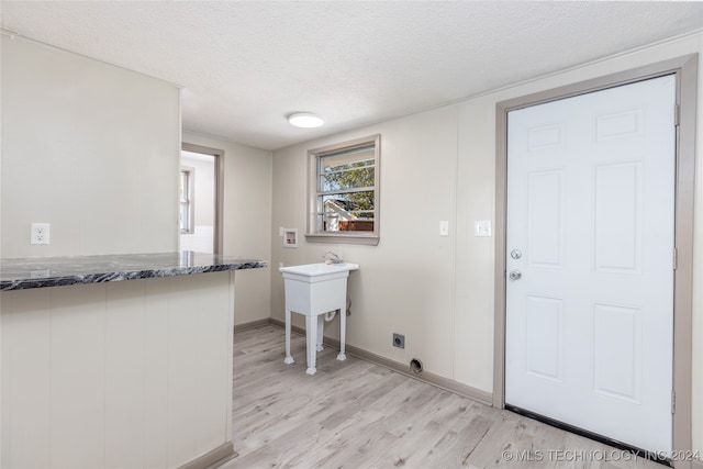 clothes washing area with light wood-type flooring, a textured ceiling, sink, electric dryer hookup, and hookup for a washing machine