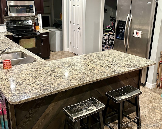 kitchen featuring light stone counters, washer / clothes dryer, appliances with stainless steel finishes, and a kitchen breakfast bar