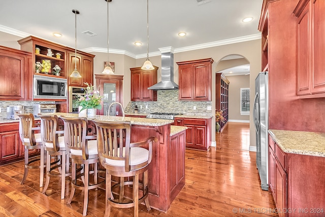 kitchen with wall chimney exhaust hood, wood-type flooring, appliances with stainless steel finishes, and decorative light fixtures