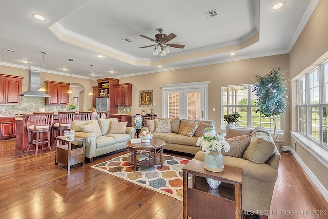 living room featuring wood-type flooring, a tray ceiling, ornamental molding, and ceiling fan