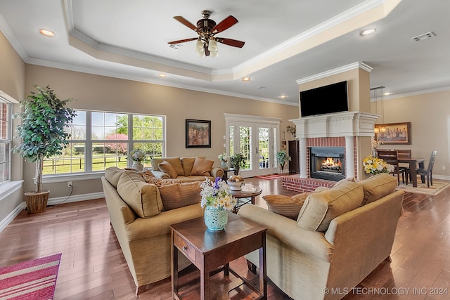 living room featuring hardwood / wood-style flooring, a tray ceiling, crown molding, and a fireplace