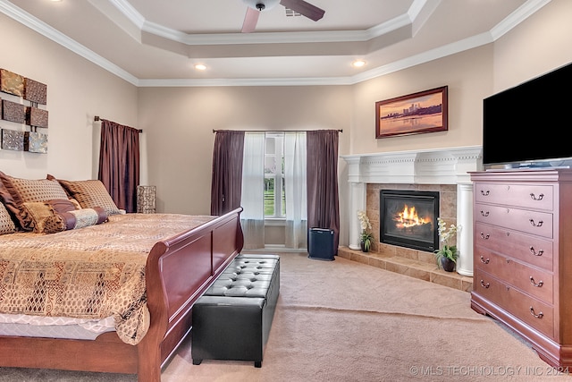 bedroom featuring a tile fireplace, light colored carpet, a raised ceiling, ornamental molding, and ceiling fan