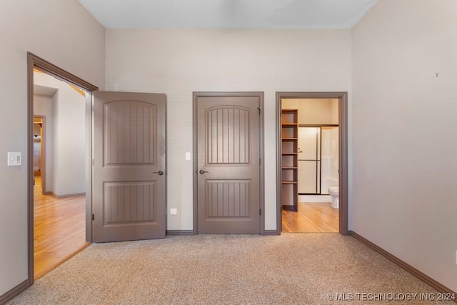 unfurnished bedroom with light hardwood / wood-style flooring, ensuite bath, and a spacious closet