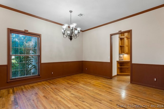 empty room with crown molding, wooden walls, an inviting chandelier, and light hardwood / wood-style flooring