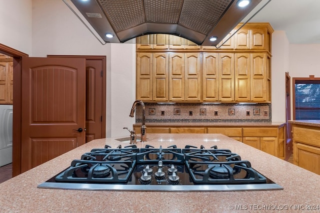 kitchen featuring backsplash, stainless steel gas cooktop, lofted ceiling, washer / dryer, and sink