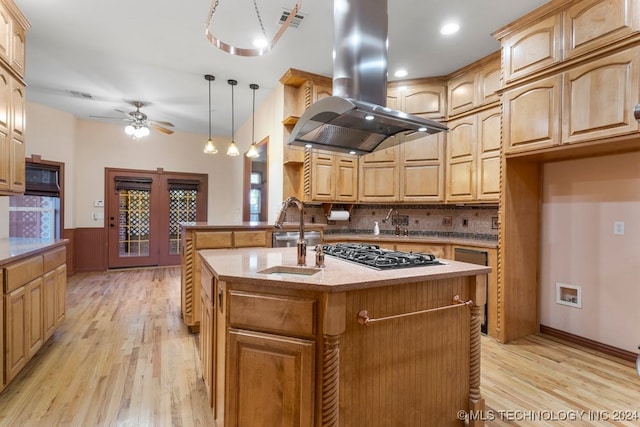 kitchen featuring an island with sink, island range hood, light wood-type flooring, decorative light fixtures, and stainless steel gas stovetop