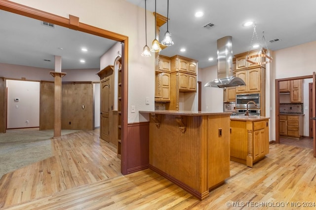 kitchen featuring kitchen peninsula, island exhaust hood, light wood-type flooring, stainless steel double oven, and a center island