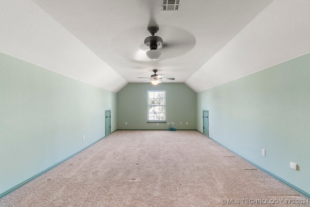 additional living space featuring a textured ceiling, vaulted ceiling, ceiling fan, and light carpet