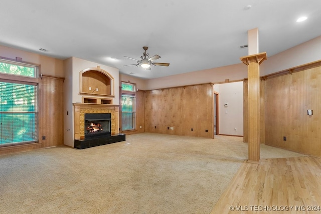 unfurnished living room with wood-type flooring, wood walls, decorative columns, and ceiling fan