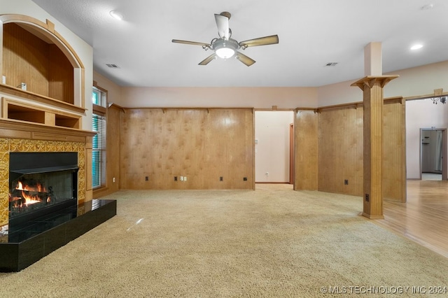 unfurnished living room with wood walls, ceiling fan, light colored carpet, and a fireplace