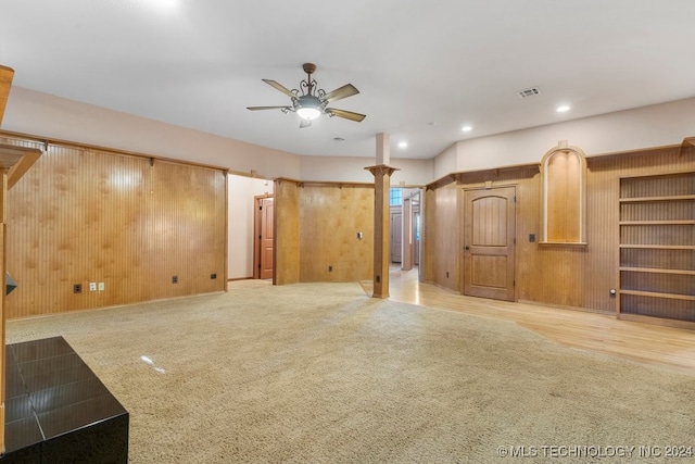 unfurnished living room featuring ceiling fan, wooden walls, and light carpet