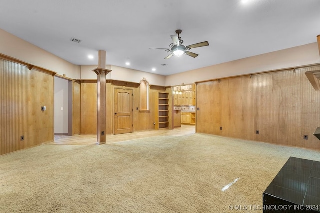 unfurnished living room with wood walls, ceiling fan, and light colored carpet