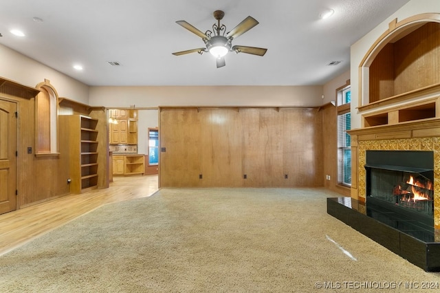 unfurnished living room featuring light hardwood / wood-style floors, a fireplace, wooden walls, and ceiling fan