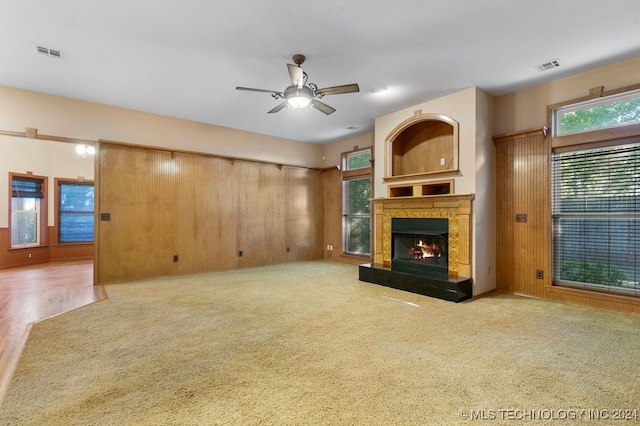 unfurnished living room featuring a high end fireplace, ceiling fan, wood walls, and light hardwood / wood-style floors