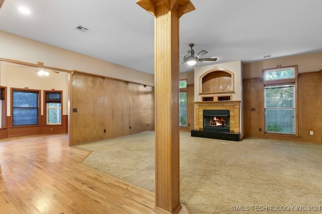 unfurnished living room with ceiling fan, light hardwood / wood-style flooring, wood walls, and decorative columns