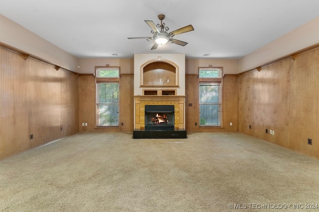 unfurnished living room featuring carpet, ceiling fan, a fireplace, and a healthy amount of sunlight