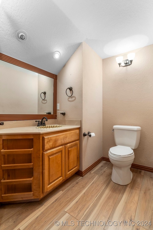 bathroom with a textured ceiling, wood-type flooring, vanity, and toilet