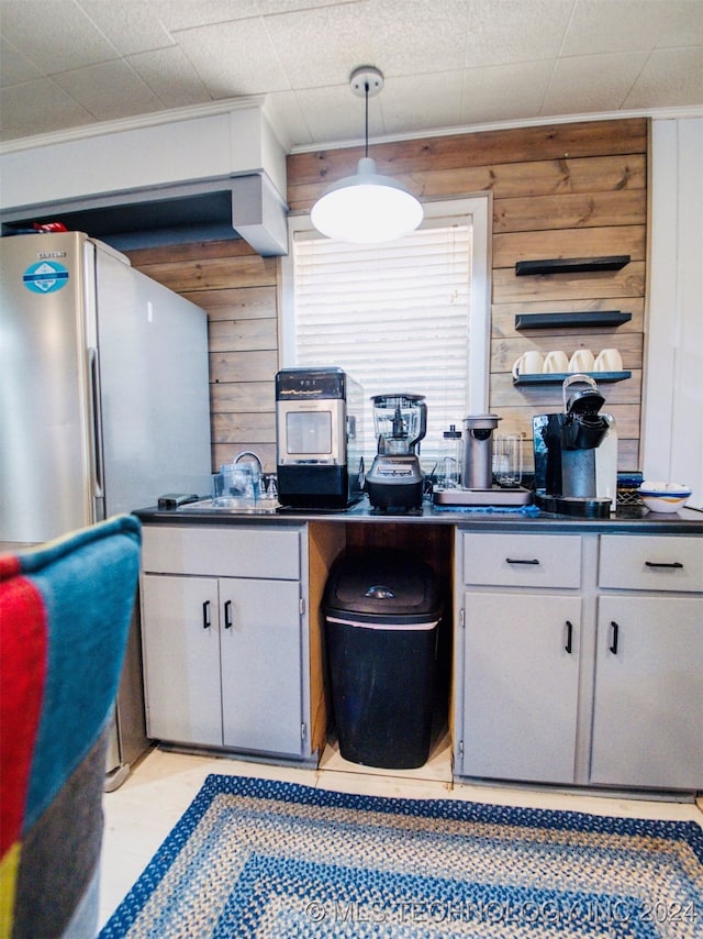 kitchen featuring decorative light fixtures, wooden walls, stainless steel fridge, and sink