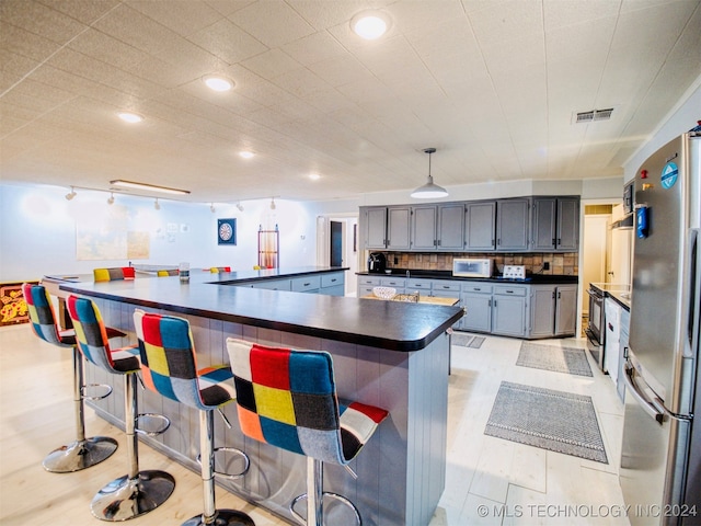 kitchen with stainless steel fridge, pendant lighting, a breakfast bar area, and backsplash