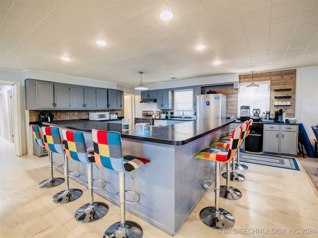 kitchen featuring stainless steel appliances, decorative light fixtures, a kitchen bar, and wooden walls