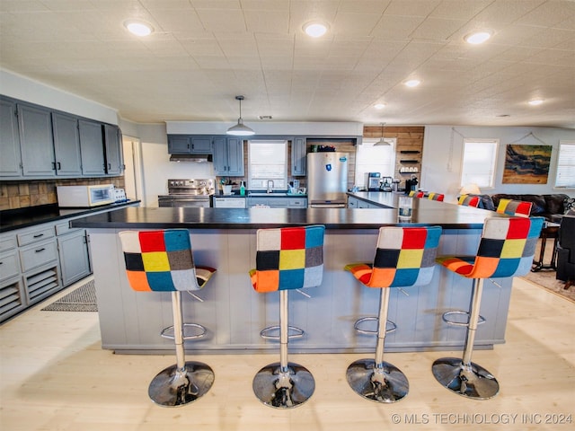 kitchen with light hardwood / wood-style floors, a large island, appliances with stainless steel finishes, and a breakfast bar