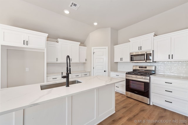 kitchen with stainless steel appliances, white cabinetry, and light stone countertops