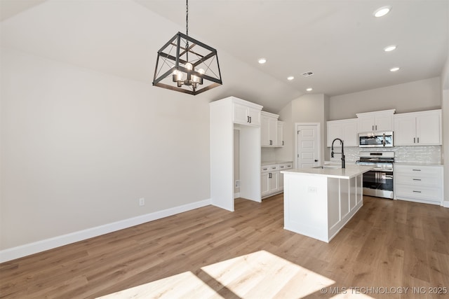 kitchen with a kitchen island with sink, hanging light fixtures, white cabinetry, stainless steel appliances, and decorative backsplash