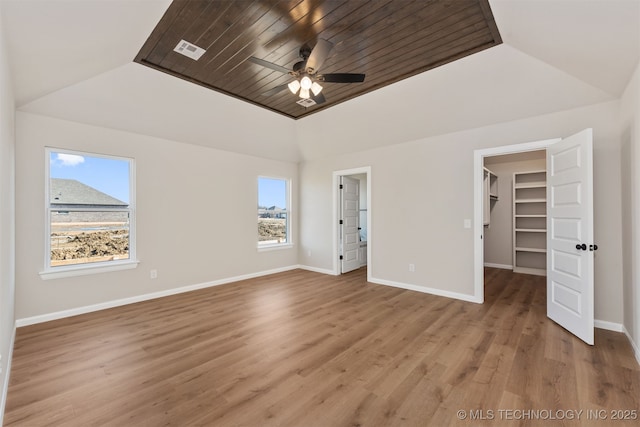 unfurnished bedroom with a walk in closet, a tray ceiling, multiple windows, and light wood-type flooring