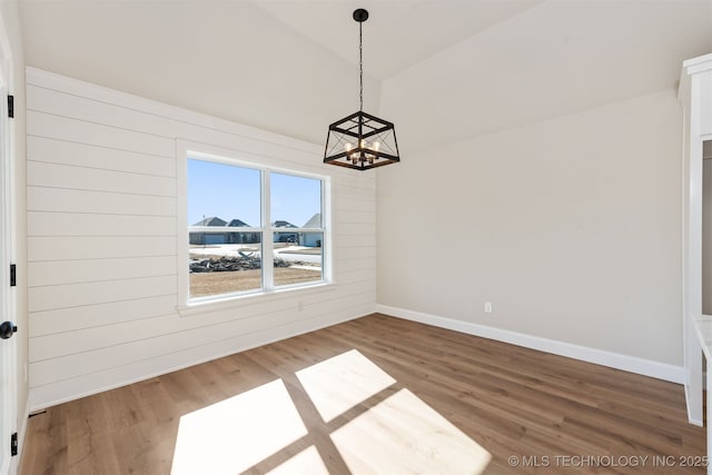 unfurnished dining area with lofted ceiling, hardwood / wood-style floors, a notable chandelier, and wood walls