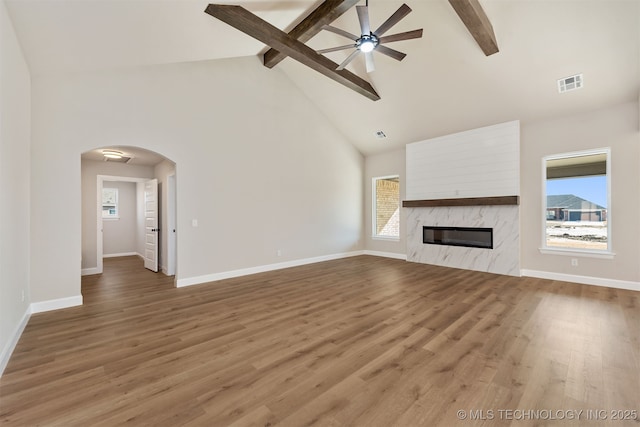 unfurnished living room featuring high vaulted ceiling, beamed ceiling, ceiling fan, a fireplace, and hardwood / wood-style floors