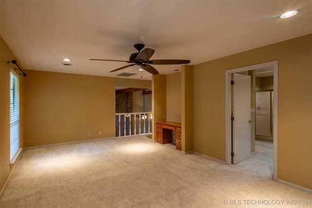 unfurnished room with light carpet, built in desk, ceiling fan, and a healthy amount of sunlight