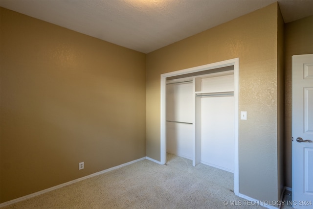 unfurnished bedroom featuring a textured ceiling, light carpet, and a closet