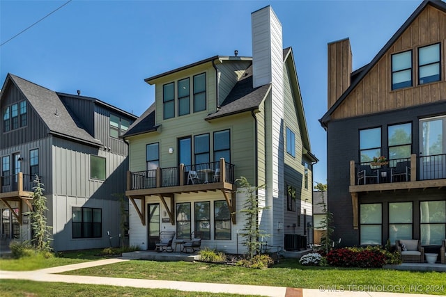 back of property with a balcony, a lawn, and central air condition unit