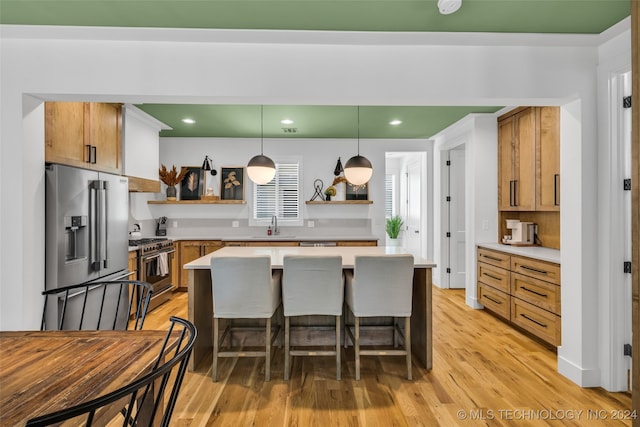 kitchen with appliances with stainless steel finishes, hanging light fixtures, a breakfast bar area, light wood-type flooring, and sink