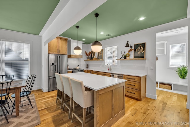 kitchen with hanging light fixtures, light hardwood / wood-style floors, a kitchen island, stainless steel appliances, and sink