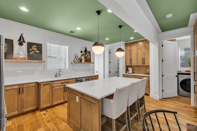 kitchen with light hardwood / wood-style floors, sink, decorative light fixtures, washer / dryer, and a kitchen bar