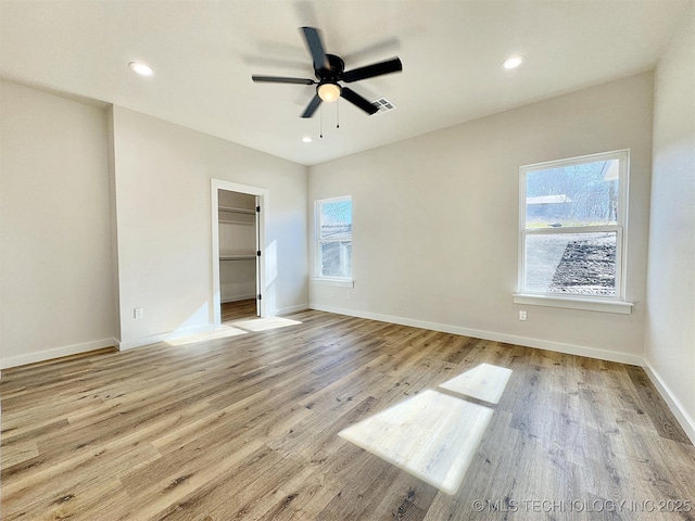 unfurnished bedroom featuring multiple windows, a walk in closet, light hardwood / wood-style floors, and ceiling fan