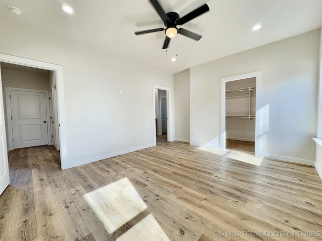 unfurnished bedroom featuring a walk in closet, a closet, ceiling fan, and light wood-type flooring