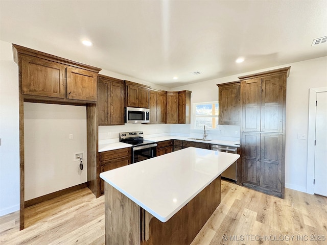 kitchen with stainless steel appliances, a kitchen island, sink, and light hardwood / wood-style flooring