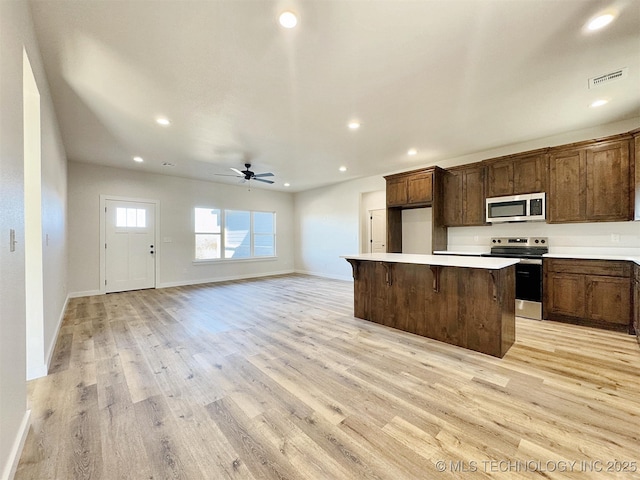 kitchen featuring light countertops, appliances with stainless steel finishes, a ceiling fan, a kitchen island, and light wood-type flooring