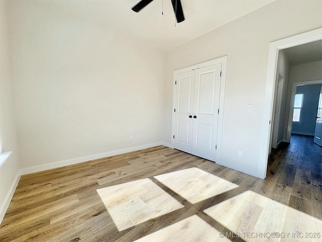 unfurnished bedroom featuring a ceiling fan, a closet, baseboards, and wood finished floors