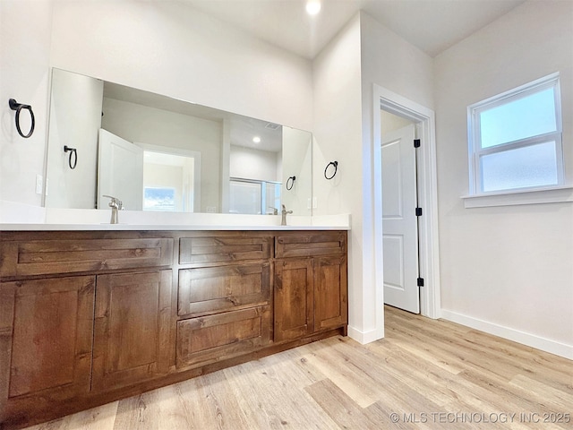 full bath featuring double vanity, a sink, baseboards, and wood finished floors